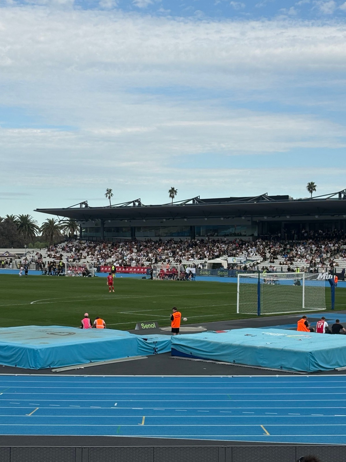 Football match in front of a full main stand at an athletics stadium