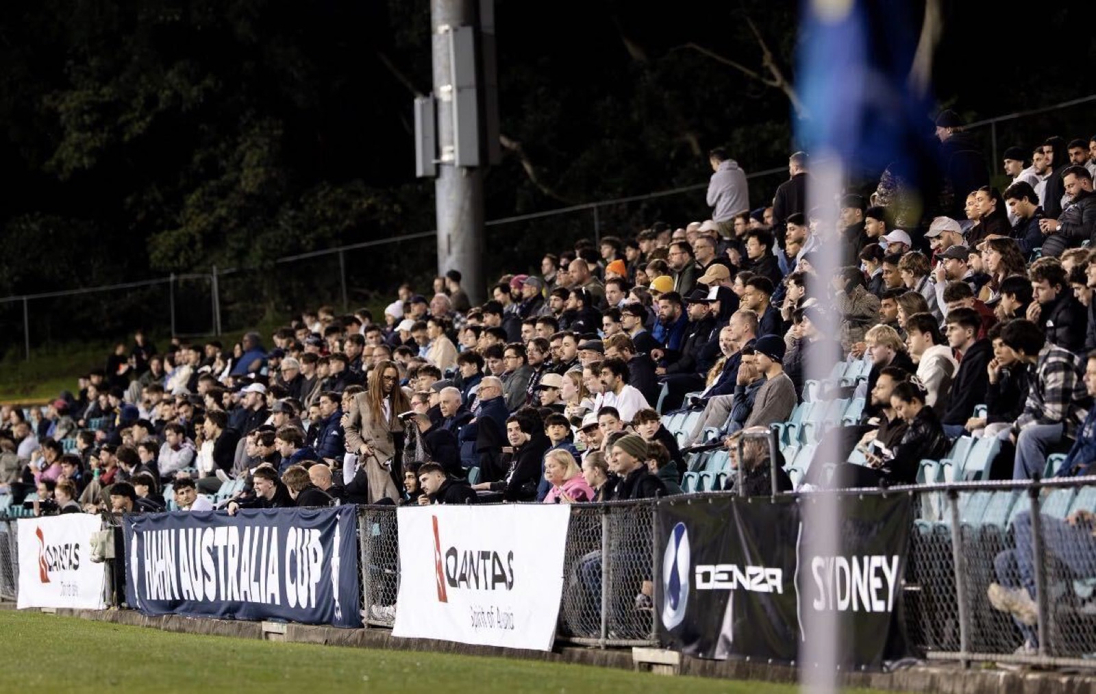 Crowd behind Hahn Australia Cup signage at a night football match